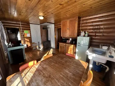 A rustic wooden cabin interior featuring a kitchen area, dining table, and a wood stove.
