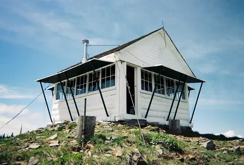 A white cabin structure on a hilltop under a blue sky.