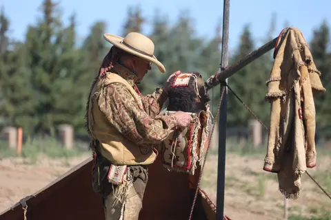 A person in traditional attire handling a decorated leather garment outdoors.