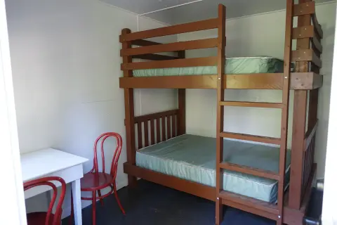 A simple room with a wooden bunk bed, a white table, and red chairs.