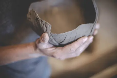A person holds an unfinished clay bowl.