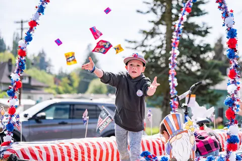 A young boy throws candy in the air from a decorated parade float.