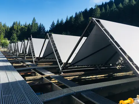 A row of triangular shade structures covers outdoor raceways beneath a blue sky and forest.