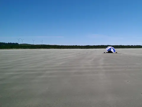 A beach with a blue and white umbrella under a clear sky.