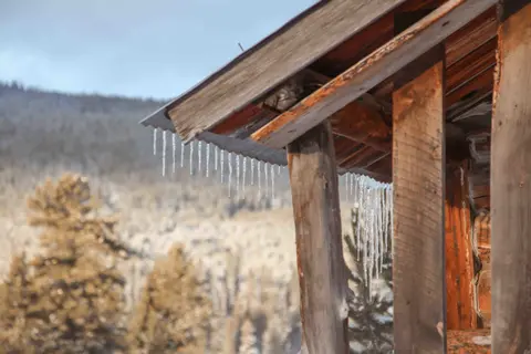 Icicles hang from the wooden roof of a rustic structure.