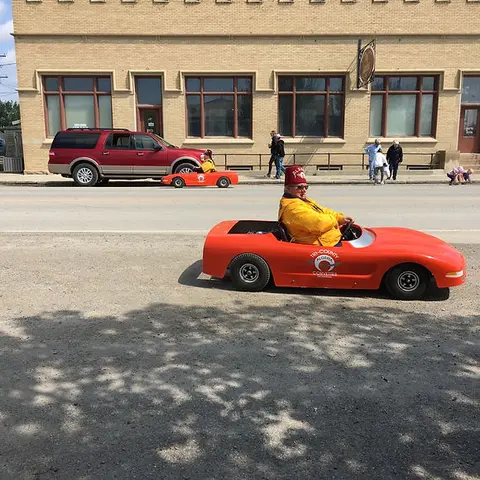 A man wearing a fez drives a small orange car on a street.