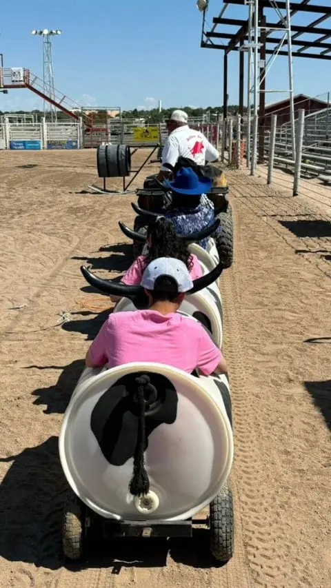 People ride in a barrel train pulled by an ATV at an outdoor arena.