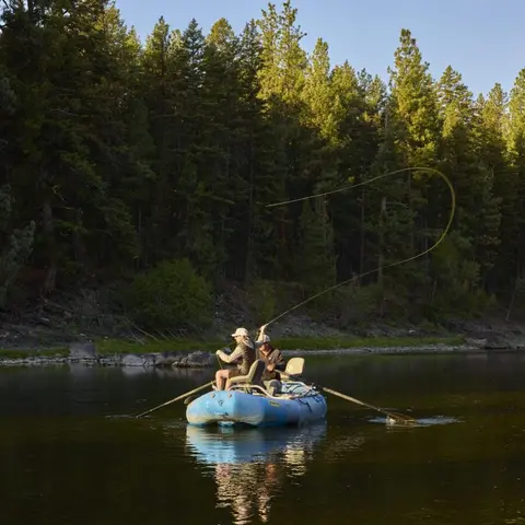 Two people fly fishing from a drift boat on a river.