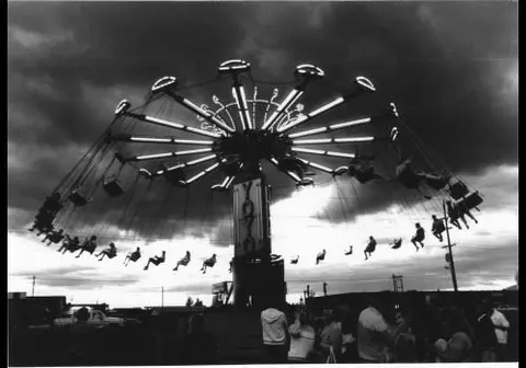 A black and white photograph of a carnival swing ride in motion.