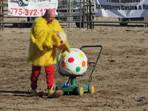 A person in a yellow costume stands with a polka-dot cart in an outdoor arena.