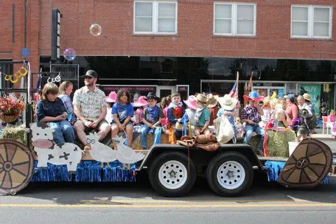 People ride on a decorated parade float in front of a brick building.