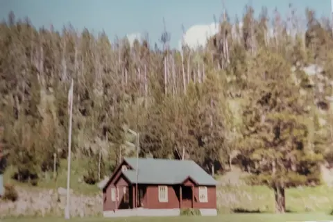 A small cabin stands before a wooded hill.