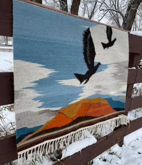 A woven textile hanging on a snowy wooden fence.
