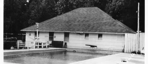 A black and white historic photo showing an outdoor swimming pool and a building.
