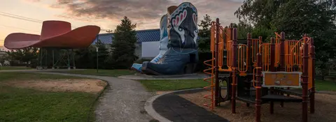 A playground with oversized cowboy boots and hat sculptures in a park.