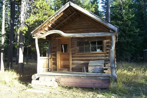 A small rustic wooden cabin sits among trees in a forest.