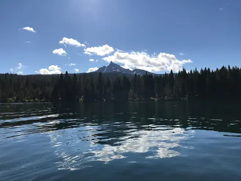 A scenic view of a lake with a mountain and forest in the background under a blue sky.