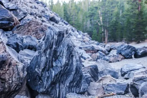 A large, textured rock stands among many other rocks in a natural setting.