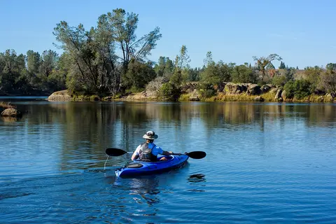 A person kayaking on a calm river surrounded by trees.