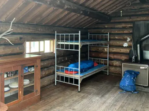 An interior view of a rustic log cabin with bunk beds and a wooden cabinet.