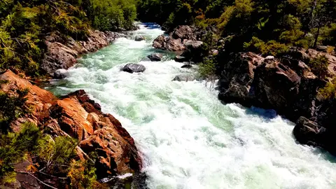 A fast-flowing river rushes through a rocky gorge surrounded by trees.