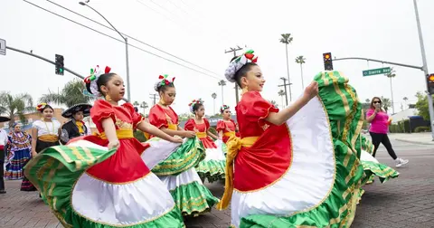 Young girls in traditional dresses perform a dance outdoors on a street.