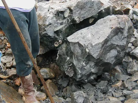 A person standing next to a large cracked rock holding a stick.