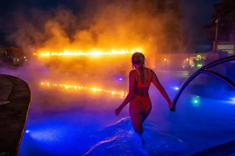 A woman stands in a brightly lit swimming pool at night.