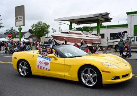 A woman waves from a yellow convertible driving down a street during a parade.