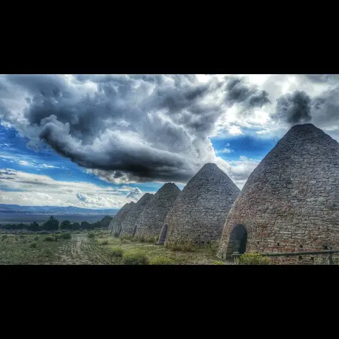 A row of stone beehive kilns stands under a dramatic cloudy sky.