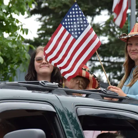 People ride in a vehicle holding an American flag.