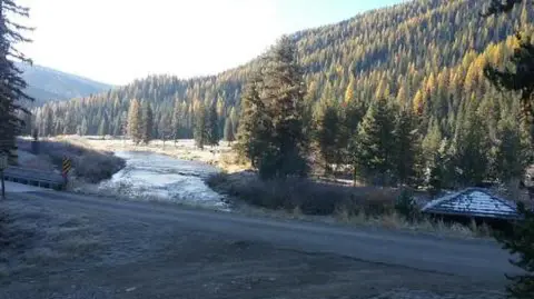 A winding river flows through a valley surrounded by a forested mountain slope.