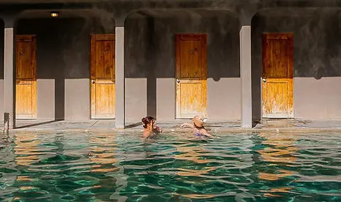 People swimming in an outdoor pool in front of a row of wooden doors.
