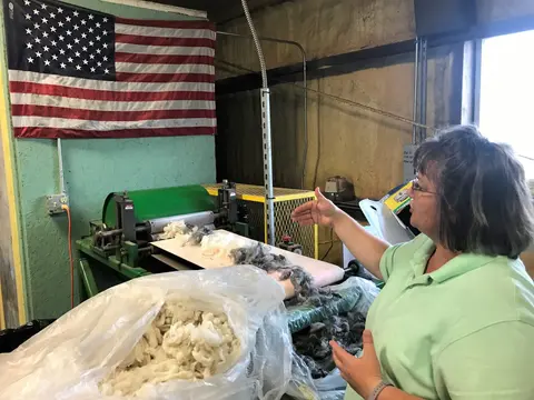 A woman demonstrates a wool processing machine inside a facility.