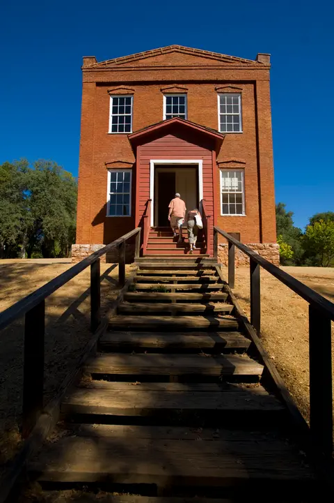 Two people walk up the wooden steps toward the entrance of a brick building.