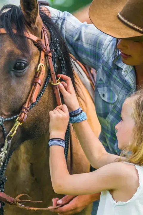 A young girl and woman adjust the bridle of a horse.