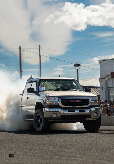 A pickup truck performs a burnout on a street.