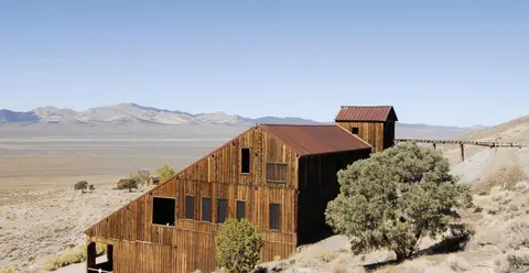 An old wooden building stands in a dry, mountainous landscape.