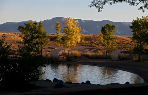 A scenic landscape showing a pond, trees, shelters, and mountains in the background.