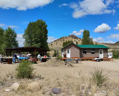 People gather near a building and a covered outdoor area on a sunny day.