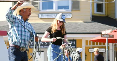 A man and a young woman practicing roping with ropes outside a building.