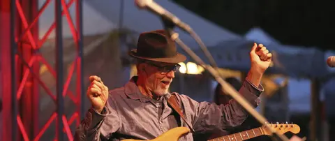 A musician wearing a hat performs on stage with a guitar.