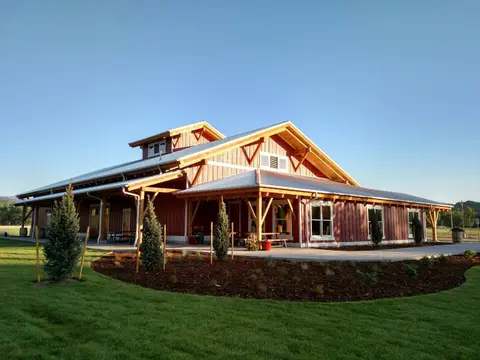 Exterior view of a large modern barn-style building with a metal roof and wooden beams under a clear blue sky.