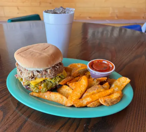 A pulled pork burger with potato wedges and a drink on a plate.