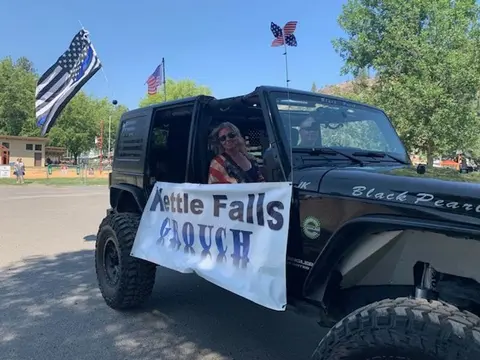 A black Jeep with a banner and flags participates in a parade.