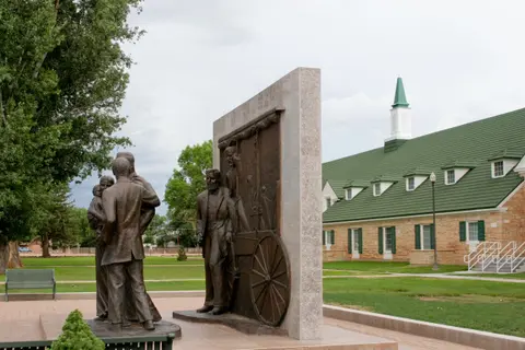 A bronze monument stands outdoors in front of a building with a green roof.