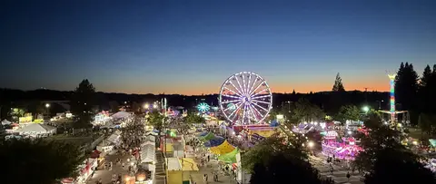 An elevated wide view of a crowded carnival at dusk with lit rides.
