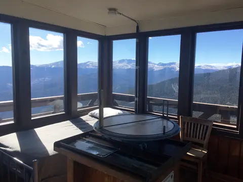 The interior of a fire lookout tower with windows looking out at mountain ranges.
