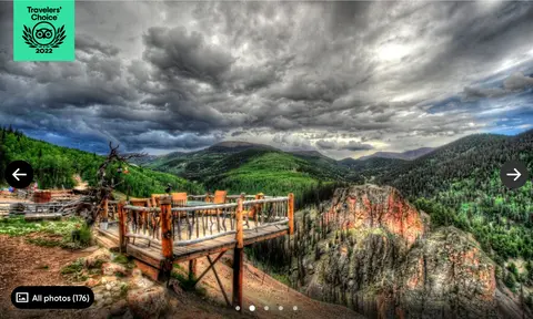 A wooden viewing platform overlooks a valley and mountainous landscape under a cloudy sky.