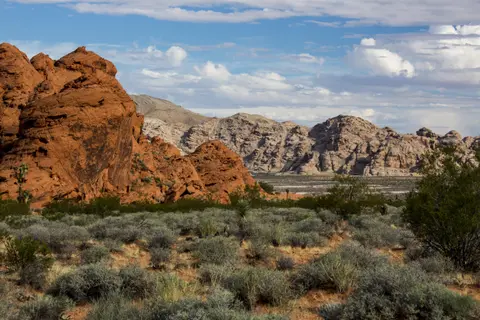A landscape featuring red rock formations and desert vegetation under a cloudy sky.